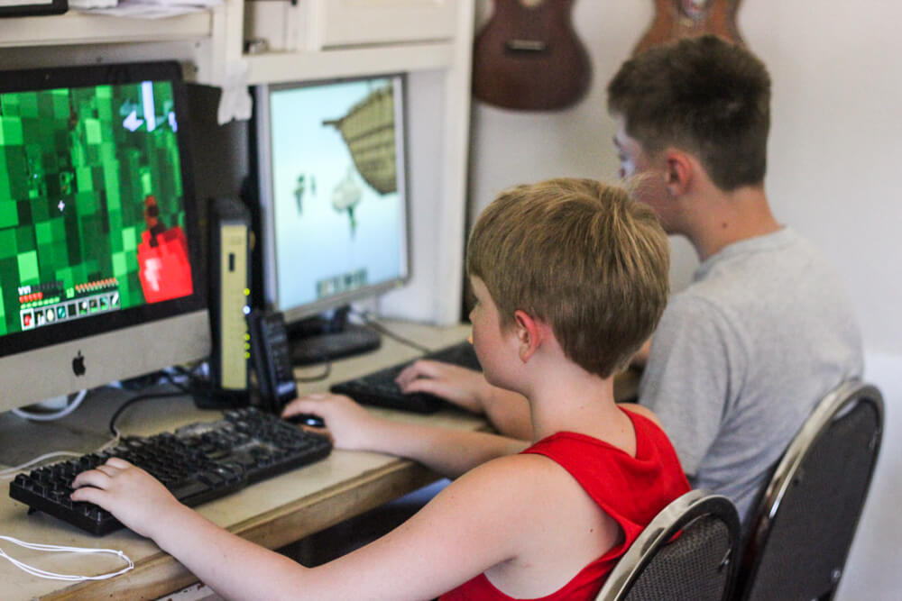child playing Minecraft on a desktop next to a child playing a computer game on a desktop