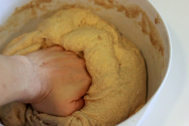 hand kneading bread dough in white bowl