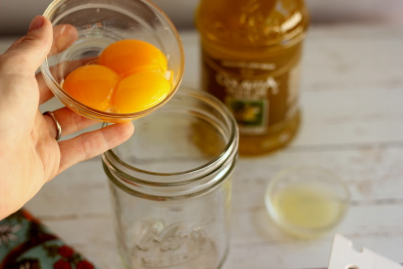 three egg yolks being poured into a small glass jar