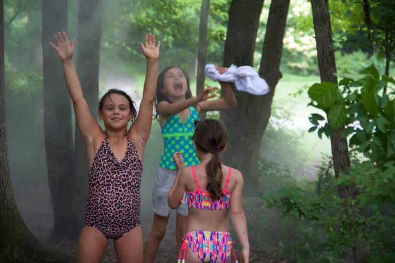 kids in swimsuits playing in water spraying from above