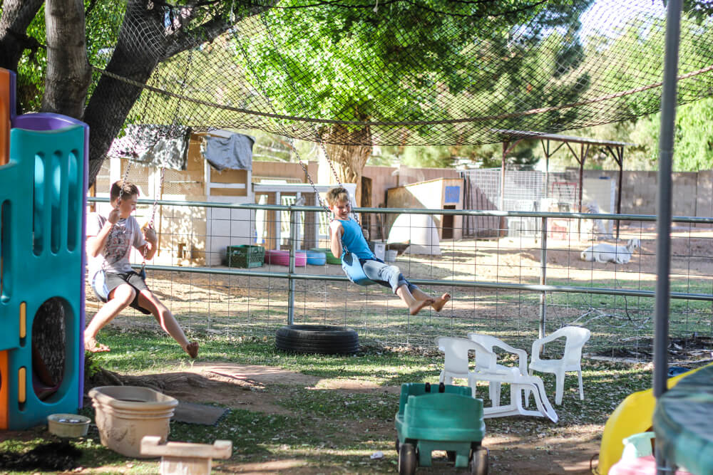 two children swinging on a swing set in a yard filled with toys