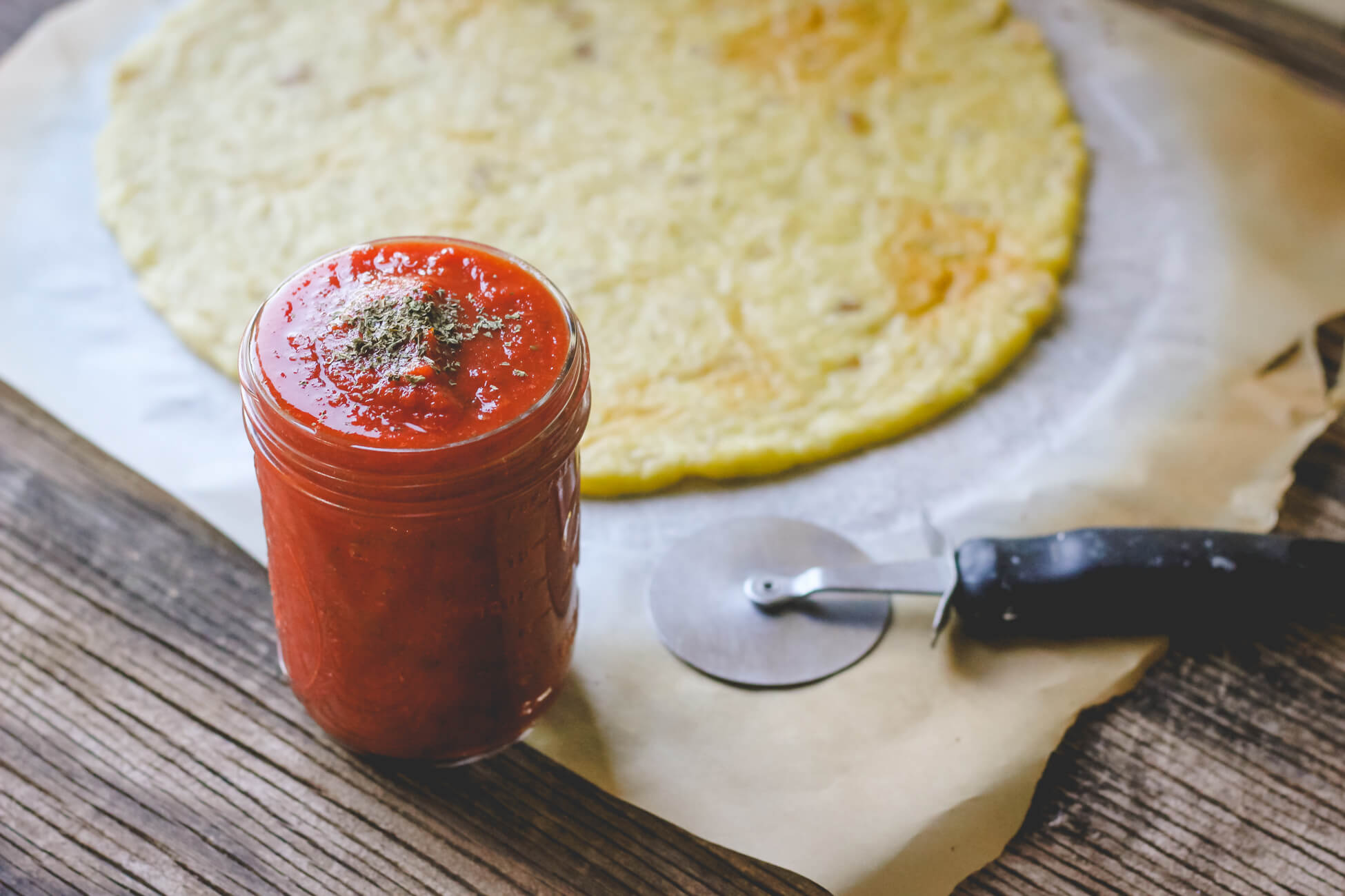 Jar of pizza sauce on wood background with pizza dough.