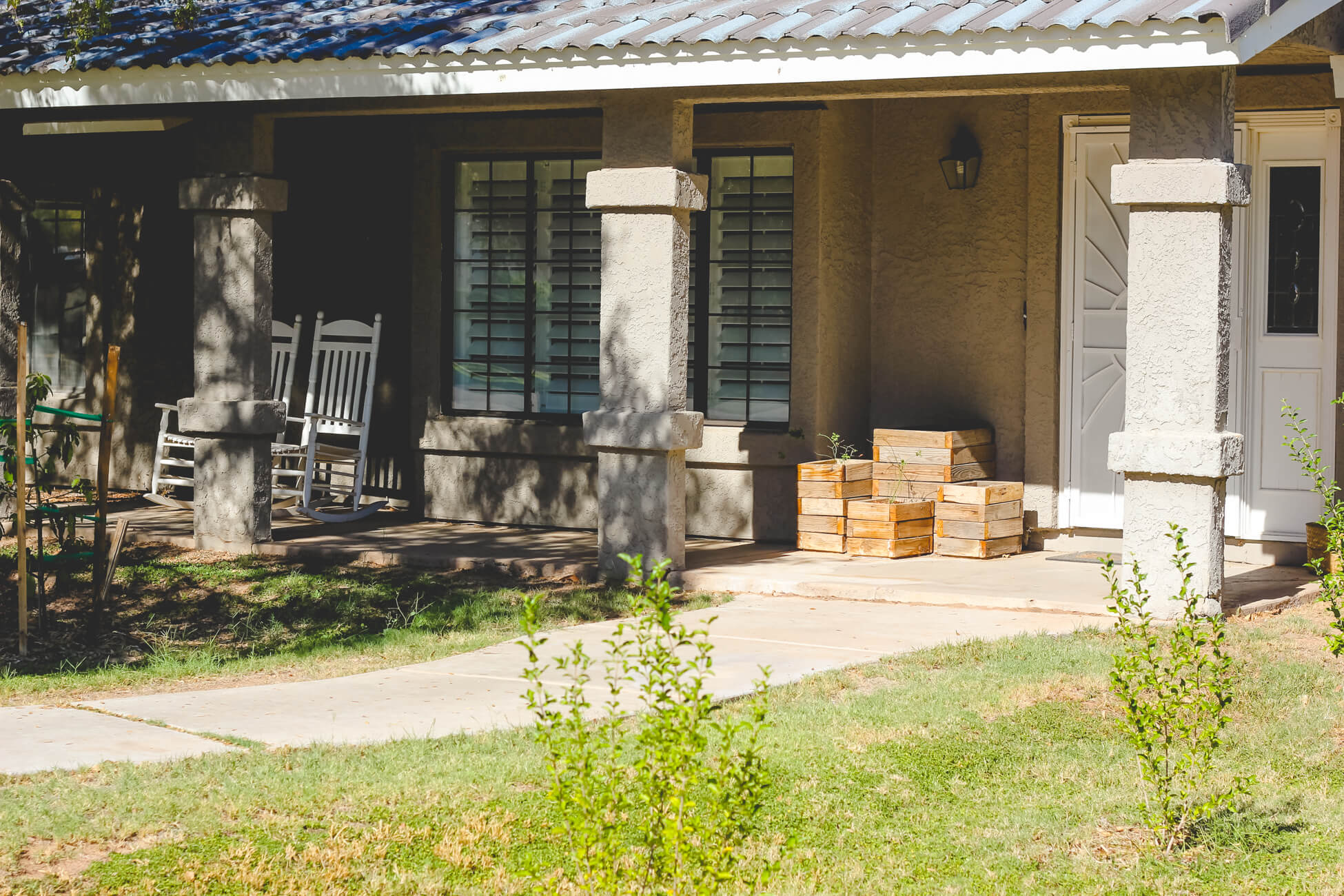 Grey farm house with planters & white rocking chairs.