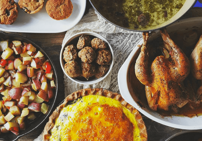 overhead shot of table with muffins, stew, cooked partridge, scones, red potatoes, baked pears and cheese souffle